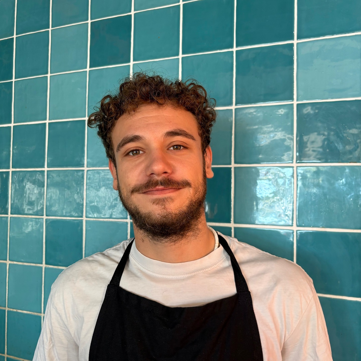 Portrait de Baptiste, chef privé, devant un mur de carrelage turquoise